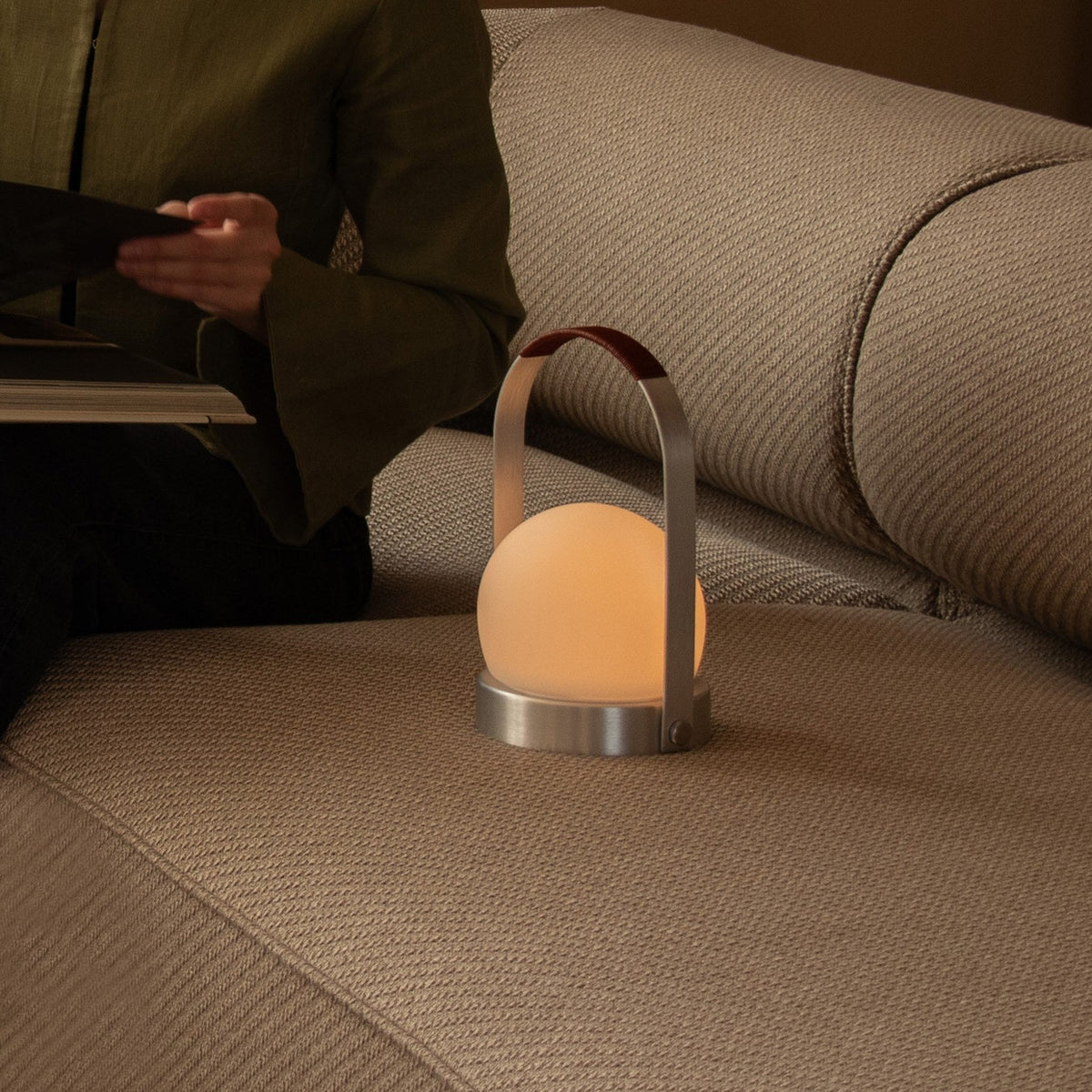 Audo Copenhagen Carrie LED Lamp Brushed Aluminium Leather lit on a sofa - KANSO#Color_Brushed Aluminium Leather