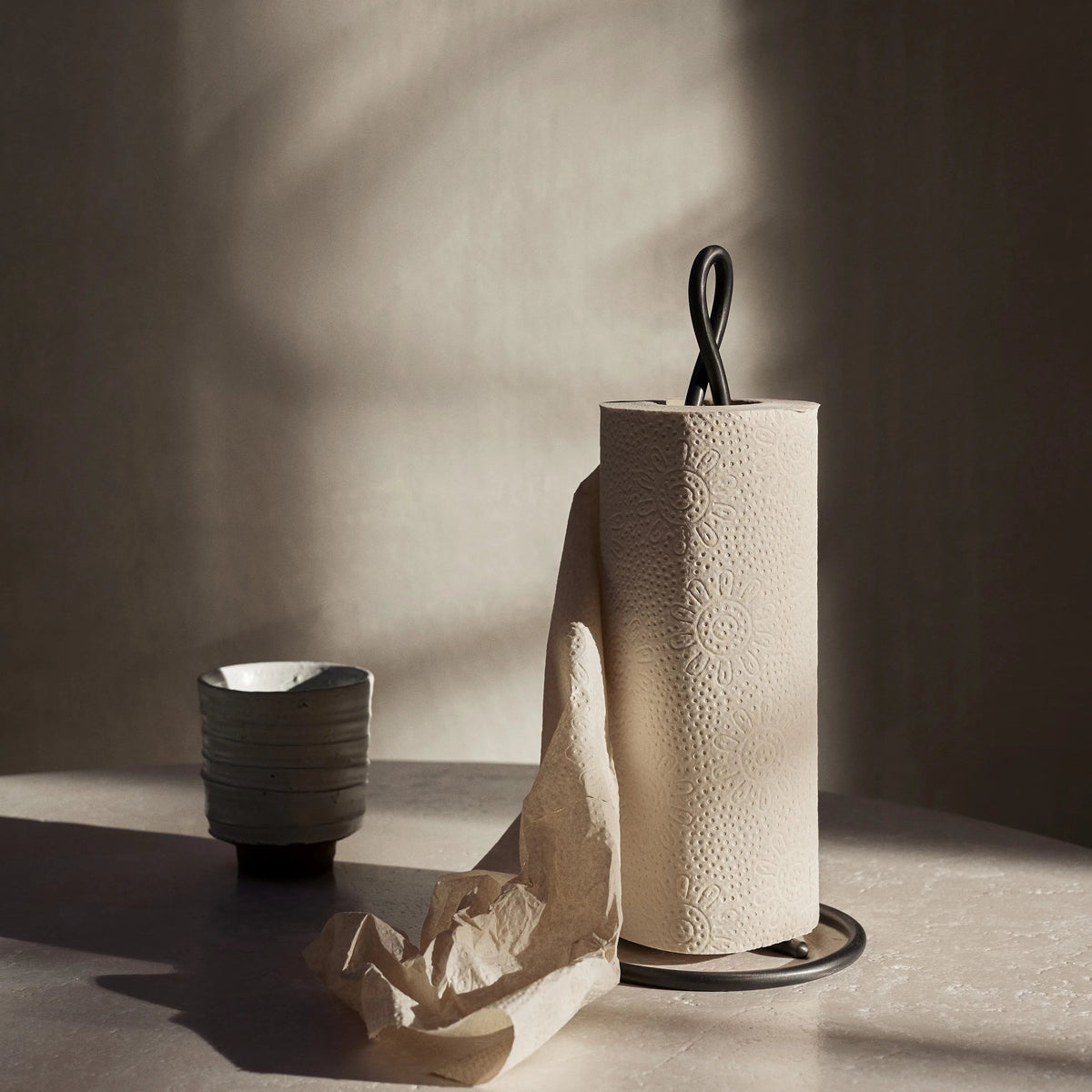 ferm Living Curvature Paper Towel Holder, Black Brass, holding a roll on a kitchen counter - KANSO#Color_Black Brass